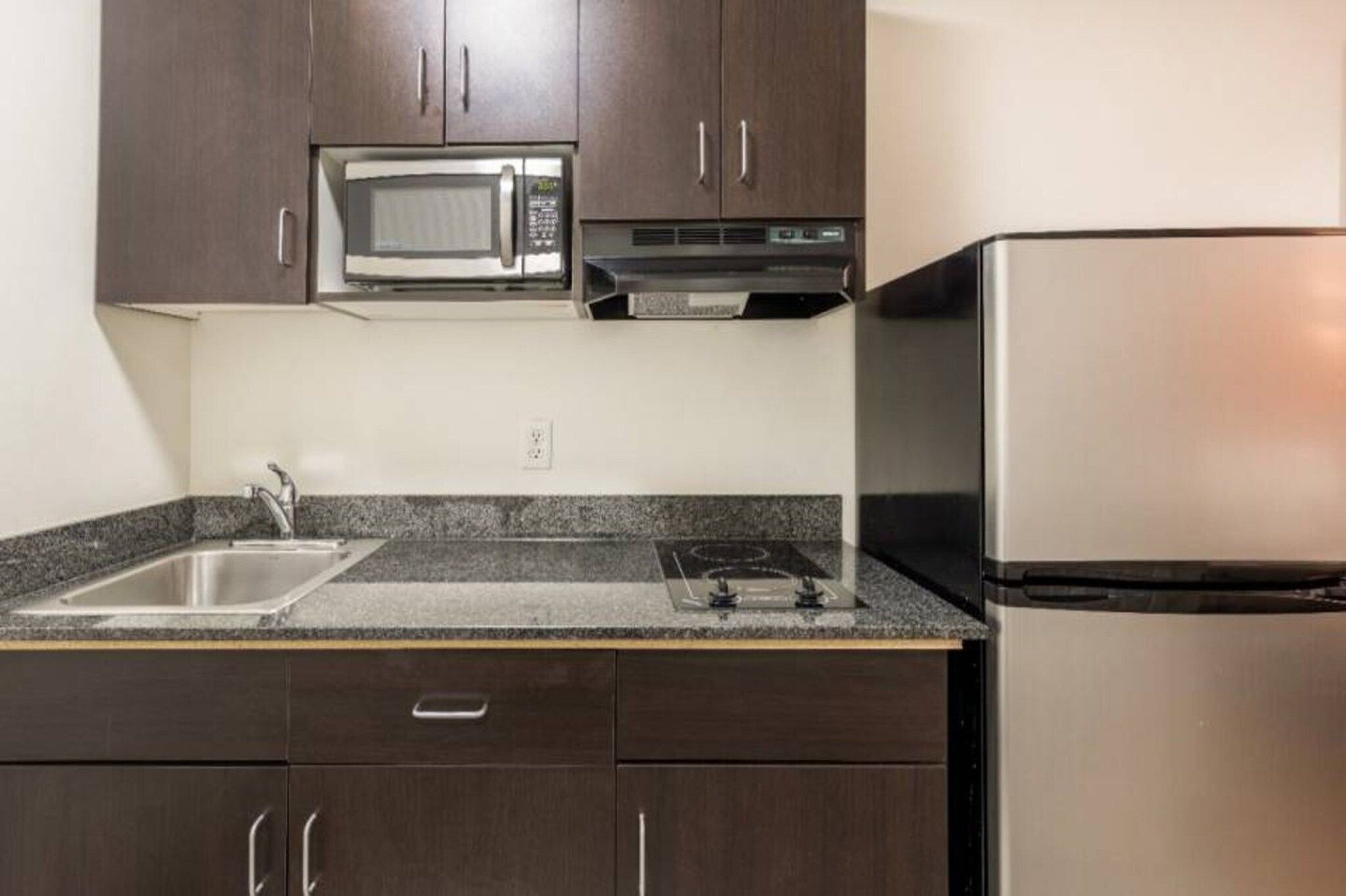 A kitchen with dark cabinets, a stainless steel refrigerator, a microwave, and a gas stove.