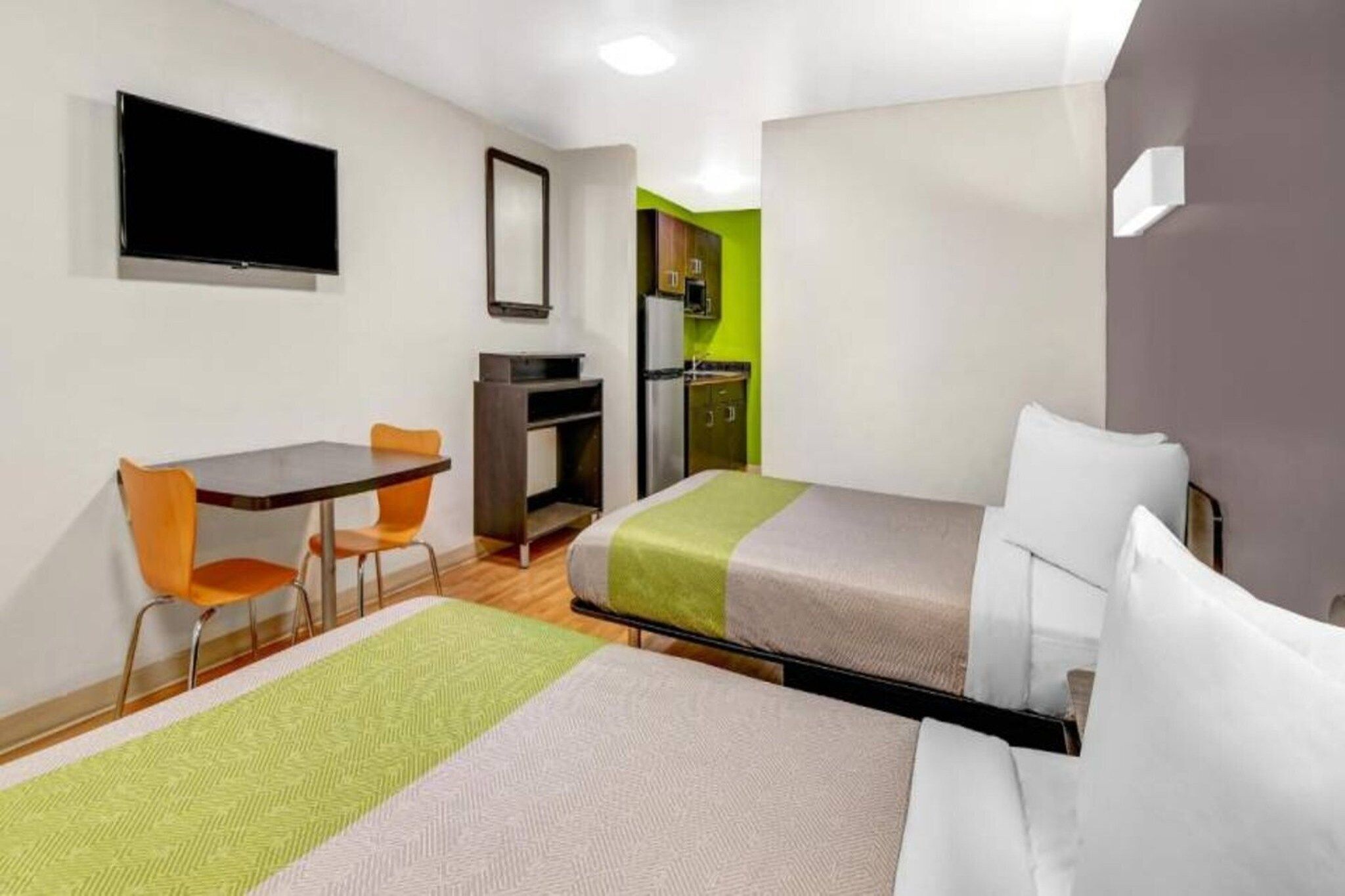 Una habitación de hotel con cama, escritorio, silla, televisor y kitchenette.