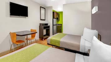 Una habitación de hotel con cama, escritorio, silla, televisor y kitchenette.