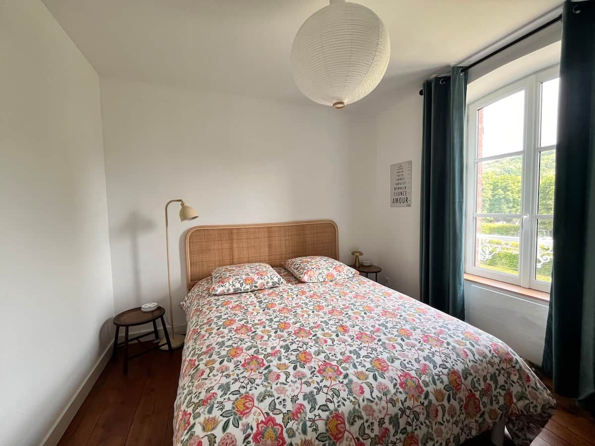 Une chambre à coucher avec une tête de lit en bois, une couvre-lit à motifs floraux, une lampe de chevet et une fenêtre avec des rideaux.