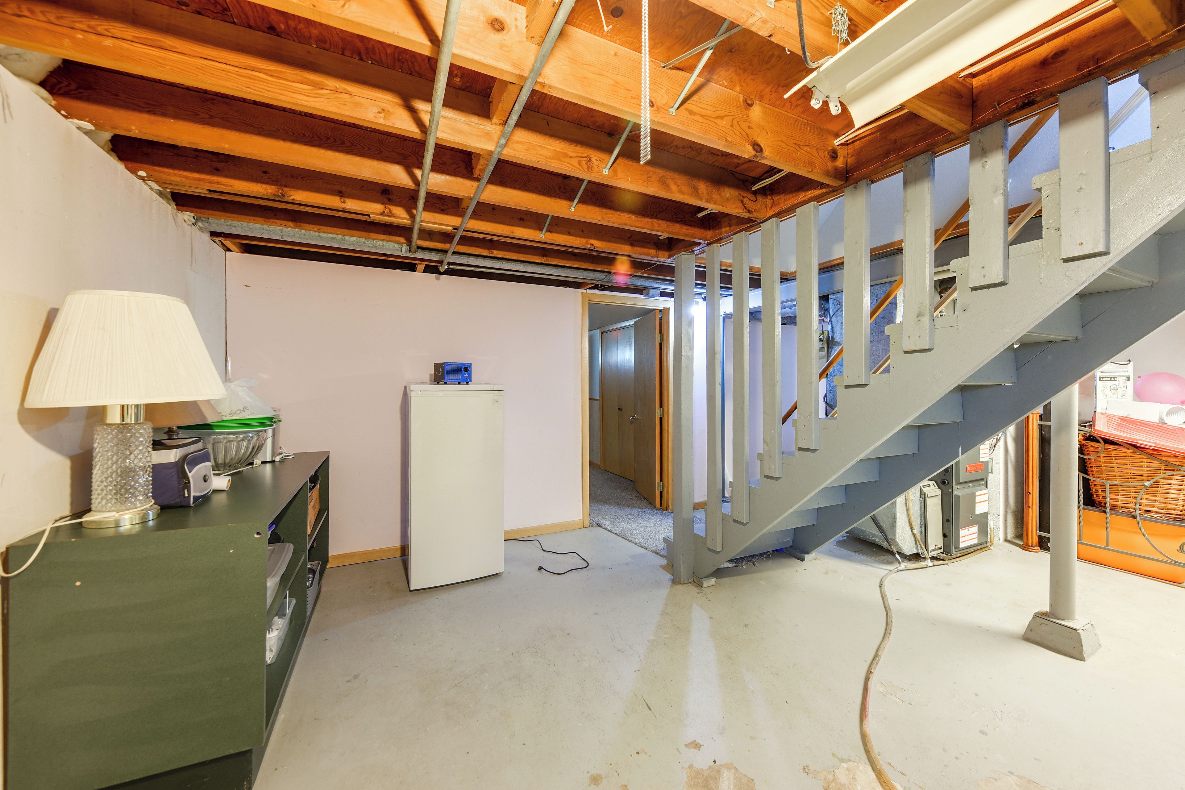 A room with a wooden ceiling, a staircase, a refrigerator, and a desk with a lamp.