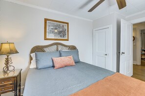 Ein Schlafzimmer mit einem Bett, einem Nachttisch, einer Lampe, einer Tür und einem gerahmten Bild an der Wand.