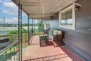 Een balkon met overkapping, met een bank en een tafel, een leuning, en uitzicht op de omgeving.