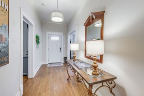 A hallway with a wooden floor, a white door, a hanging plant, a mirror with a lamp, and a glass-top table with a tray. - Pet Friendly Near UAB in Forest Park/East Avondale (Birmingham)