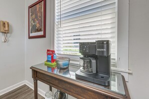 Eine Kaffeemaschine steht auf einem Glastisch, zusammen mit einem gerahmten Bild und einem Telefon an der Wand.