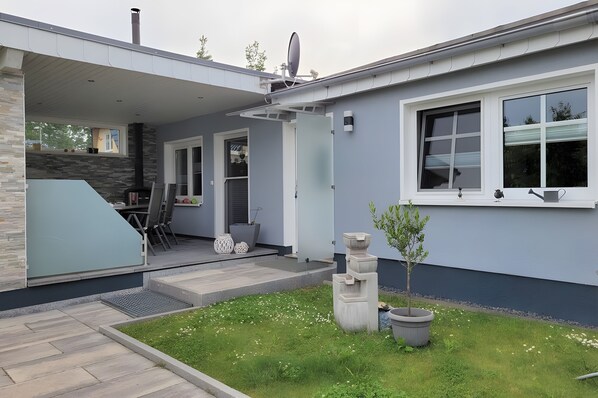 A modern house with a covered patio, a stone fireplace, and a small garden with potted plants.