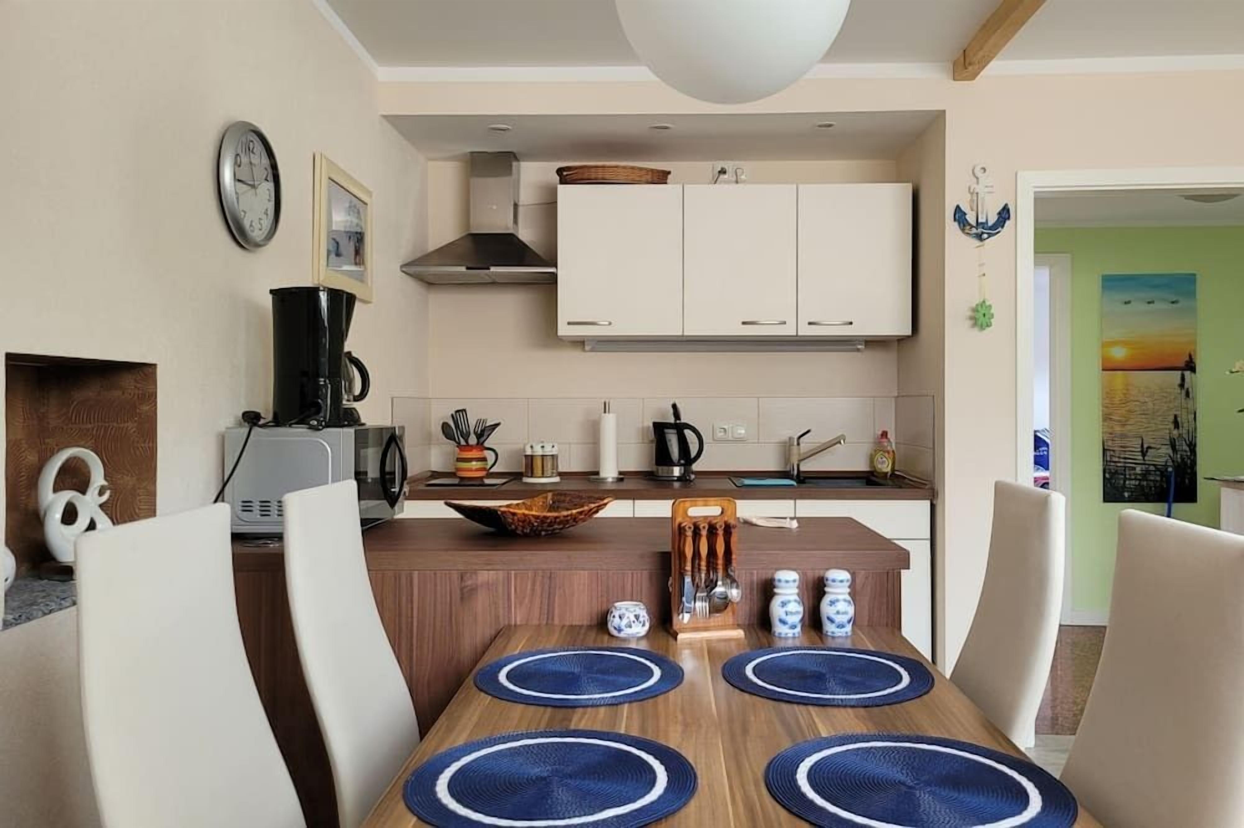 Eine moderne Küche mit weißen Schränken, einer Kaffeemaschine und einem Essbereich mit einem Holztisch und Stühlen.