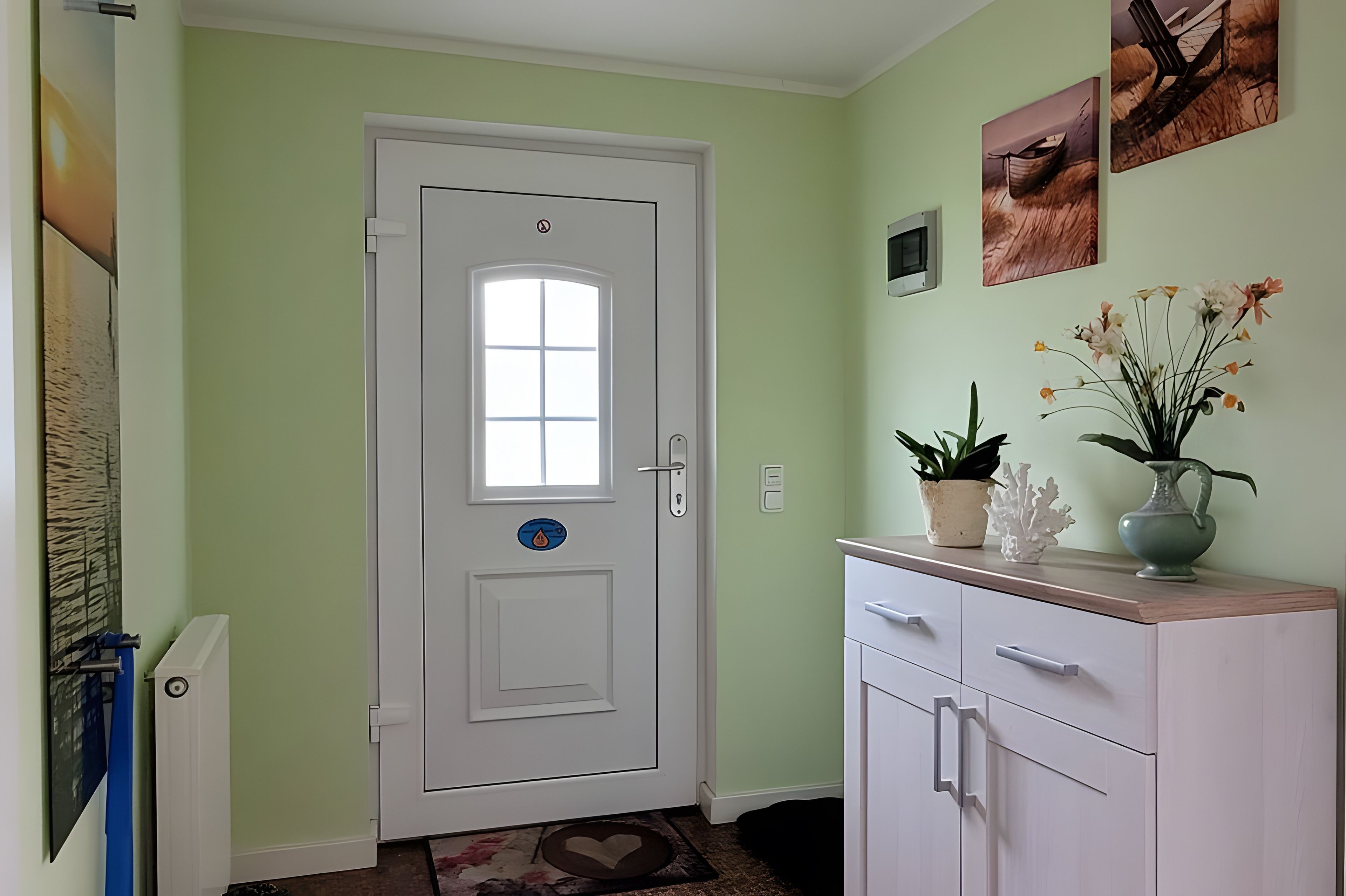 Une pièce avec une porte blanche, une petite plante en pot, un vase rempli de fleurs et un tableau accroché au mur.