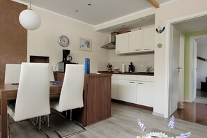 A modern kitchen with white cabinets, a wooden dining table, and a coffee machine. - Apartment 'Ferienwohnung Zeitlos' (Stralsund)