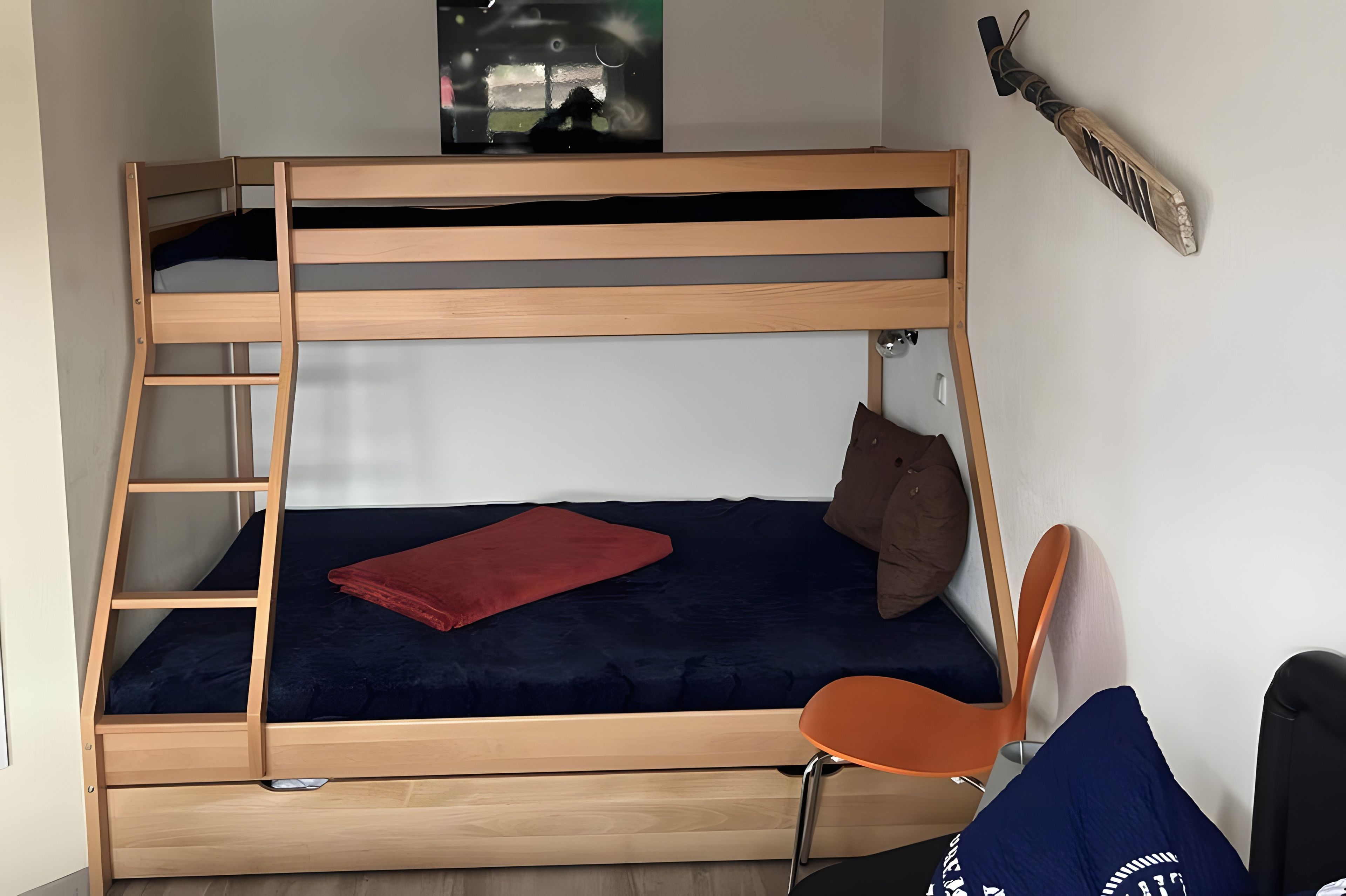 Ein Etagenbett mit einer Leiter, ein Einzelbett mit einer roten Decke, ein braunes Kissen und ein Stuhl.