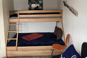 A bunk bed with a ladder, a single bed with a red blanket, a brown pillow, and a chair. - Apartment 'Ferienwohnung Zeitlos' (Stralsund)