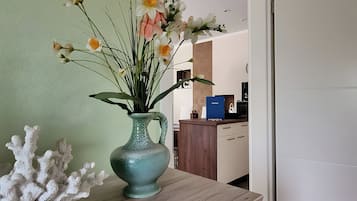 Un vaso con fiori su un tavolo di legno in una stanza con una parete verde e un'area cucina sullo sfondo.