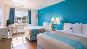 Ett hotellrum med två sängar, ett skrivbord och ett fönster med gardiner.