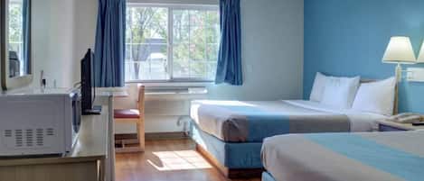 A hotel room with a bed, a desk with a computer, a chair, a window with curtains, and a lamp.
