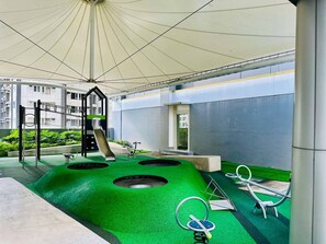 An outdoor play area with a slide, swings, and a climbing structure under a canopy. - Royal Fame Residence (Mandaluyong City)