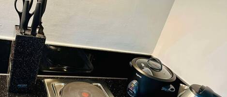 A kitchen with a black countertop, a stove with two burners, a kettle, and a pair of scissors in a holder.