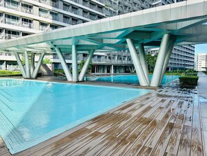 A swimming pool with a wooden deck, surrounded by a modern building with balconies. - Royal Fame Residence (Mandaluyong City)