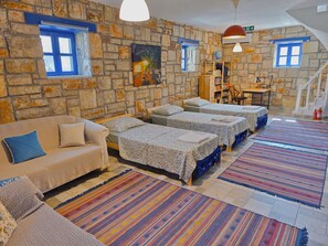 A room with a stone wall, a sofa, three beds, a desk, and a staircase.