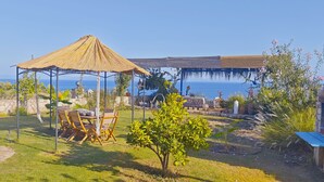 A patio with a thatched gazebo, outdoor furniture, and a view of the sea. - Pietra & Mare – Authentic Stone Villa Sea & Nature (Milas)