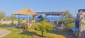 A patio with a thatched gazebo, outdoor furniture, and a view of the sea.