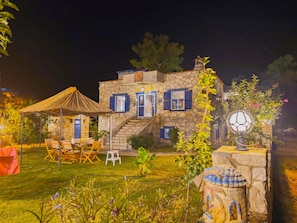 A stone house with a thatched roof, outdoor seating, and a decorative lantern.