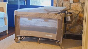 A baby crib with a canopy labeled 'Withme II' and 'KANZ' in a room with a stone wall and a blue door.