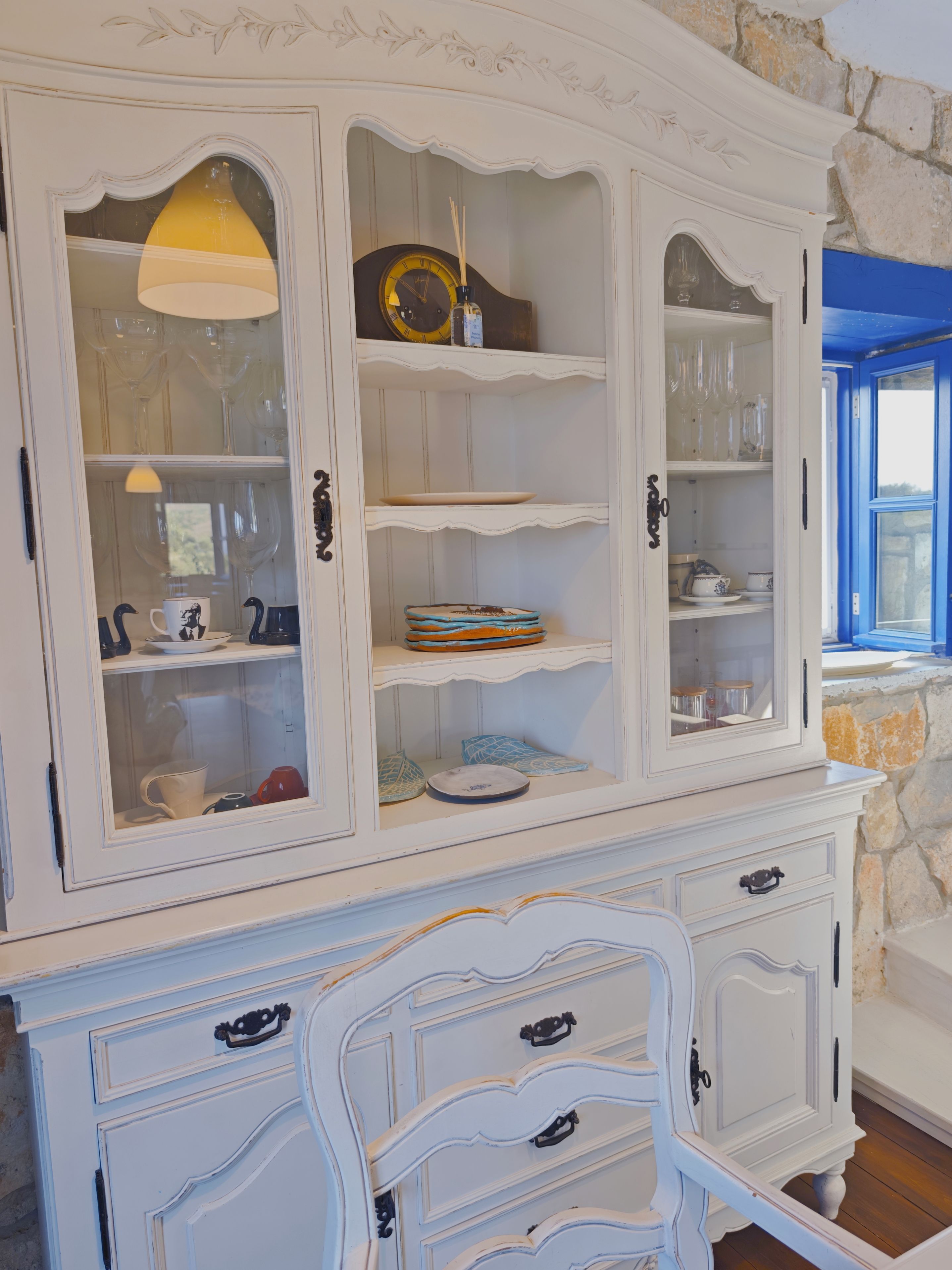 Een witte kast met glazen deuren, gevuld met servies en ander glaswerk.