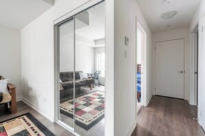 A modern apartment with a sliding glass door leading to a living area, a hallway with a door, and a visible bed with a patterned rug. - Cozy one bed town house to explore city (Toronto)