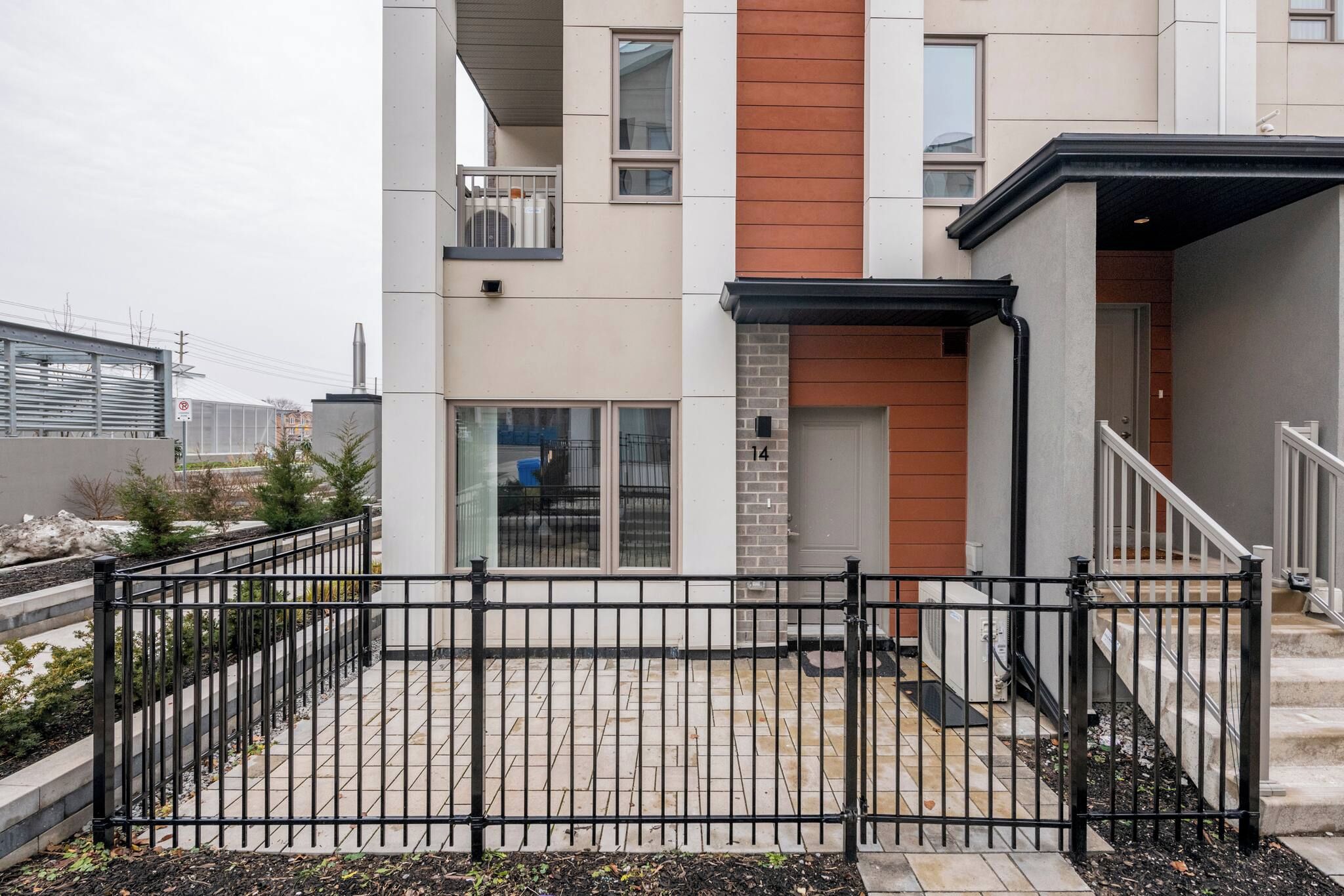 A modern residential building with a fenced backyard, a visible number '14' on the facade, and a staircase leading to the entrance.