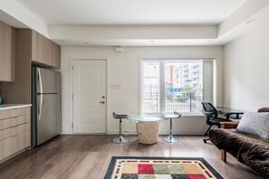 A compact kitchen with a refrigerator, a dining area with two chairs and a glass table, and a sofa with a patterned throw. - Cozy one bed town house to explore city (Toronto)
