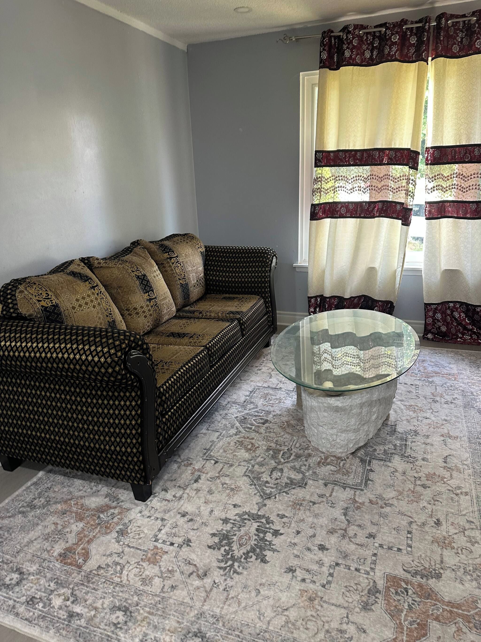A room with a patterned sofa, a glass coffee table, and patterned curtains.