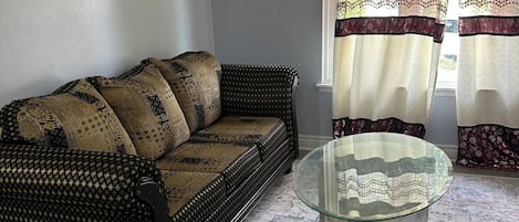 Une pièce avec un canapé à motifs, une table basse en verre et des rideaux à motifs.