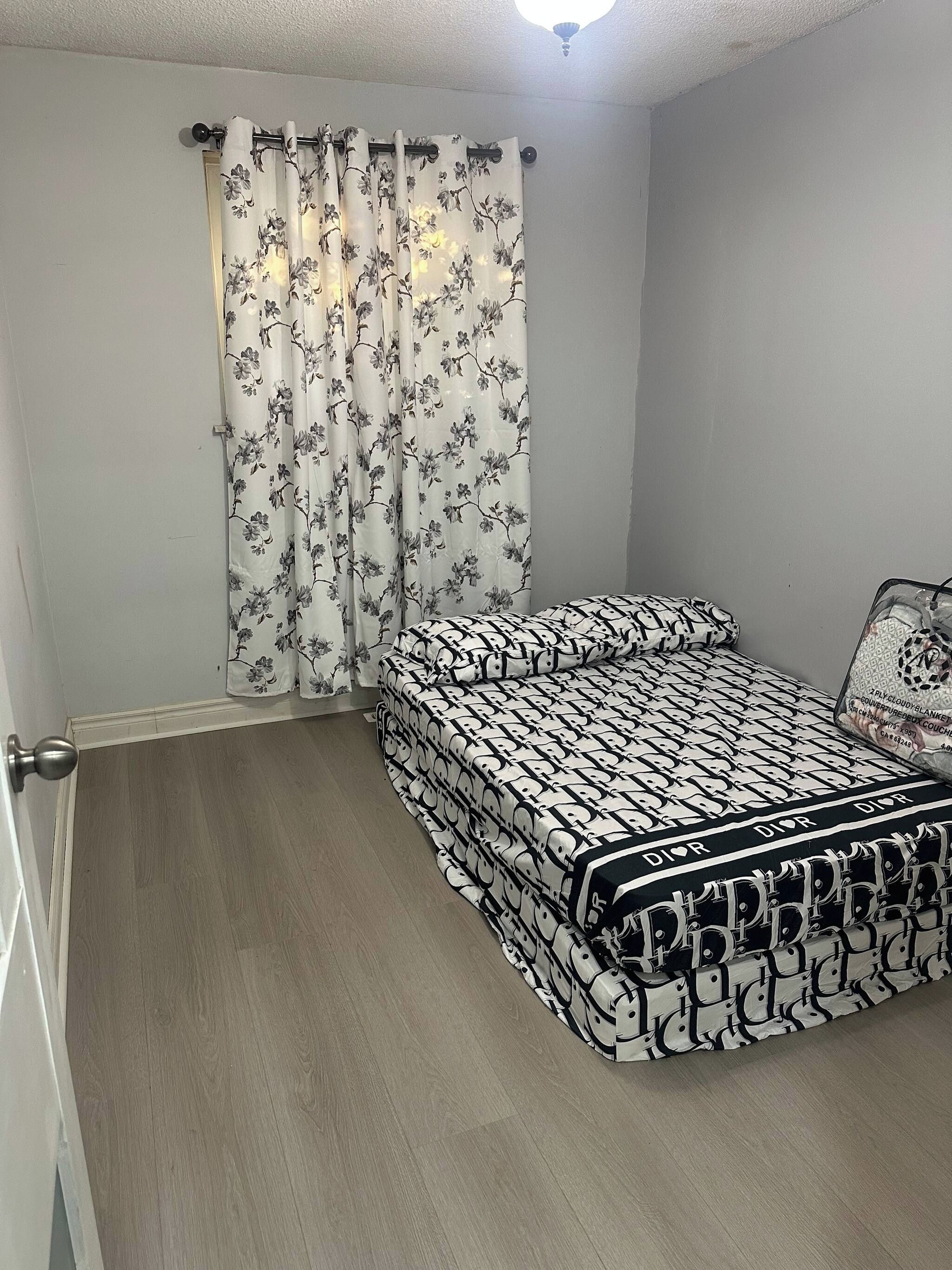 Ein Schlafzimmer mit einem Einzelbett, einer Tür und einem Fenster mit floralem Vorhang.