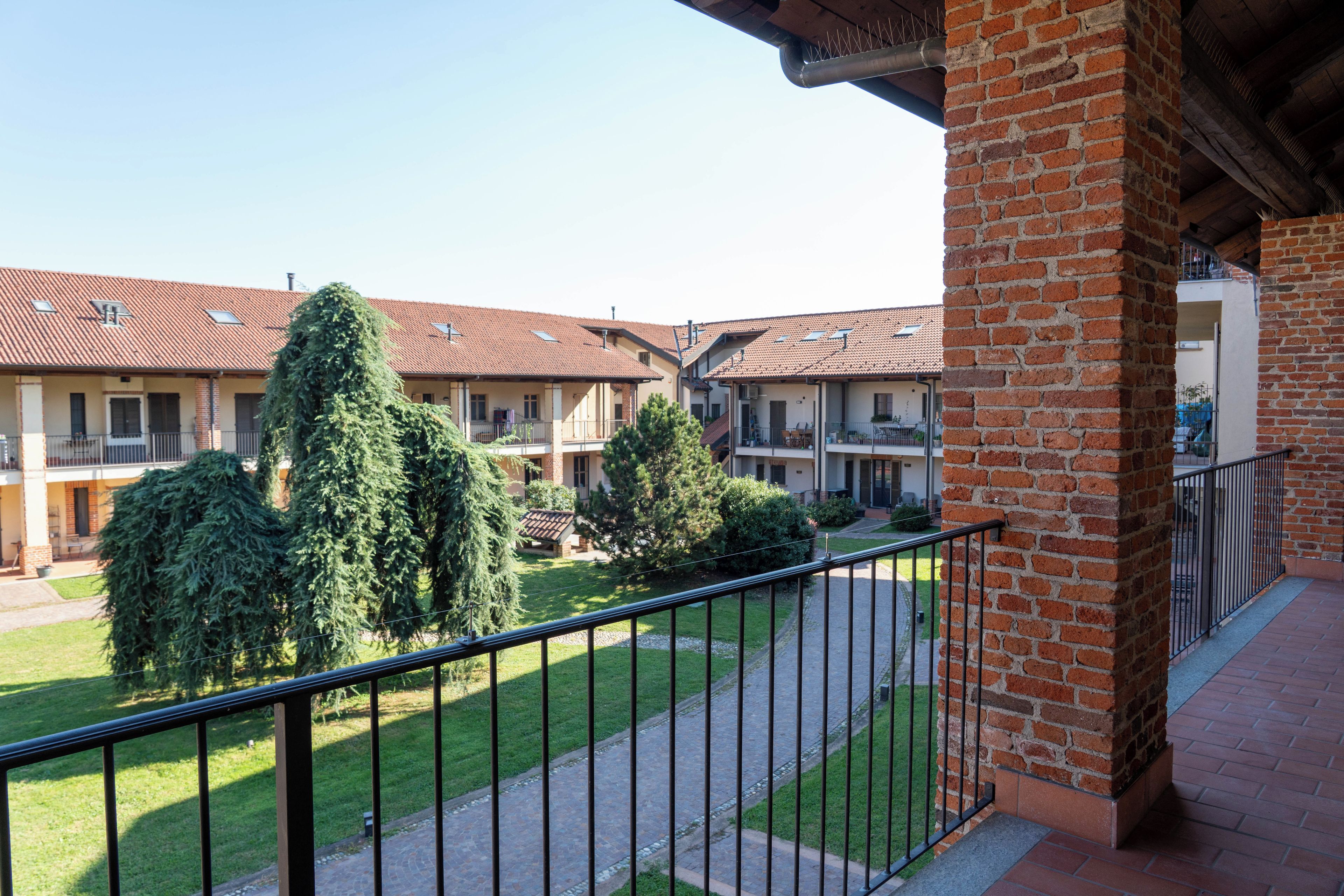 A courtyard with a brick building, a paved walkway, and a metal railing.