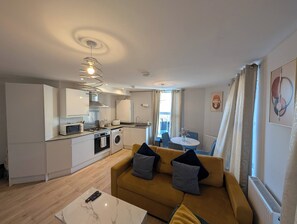 A compact living space with a kitchenette, a sofa with cushions, a dining area, and a view through a window. - Harbour Haven Dover Road Folkestone (Kent)