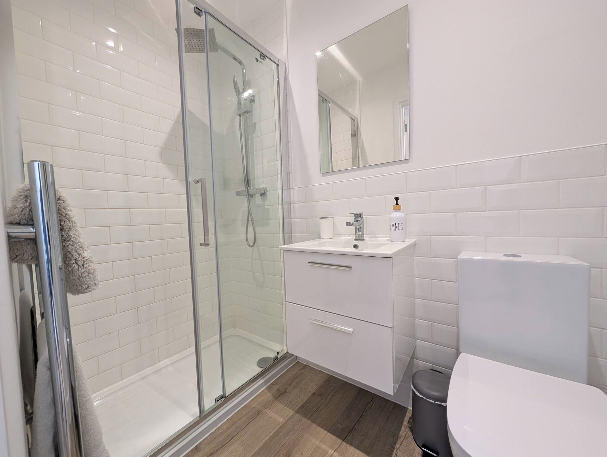 A modern bathroom with a glass shower enclosure, a white sink with a mirror above, and a toilet.