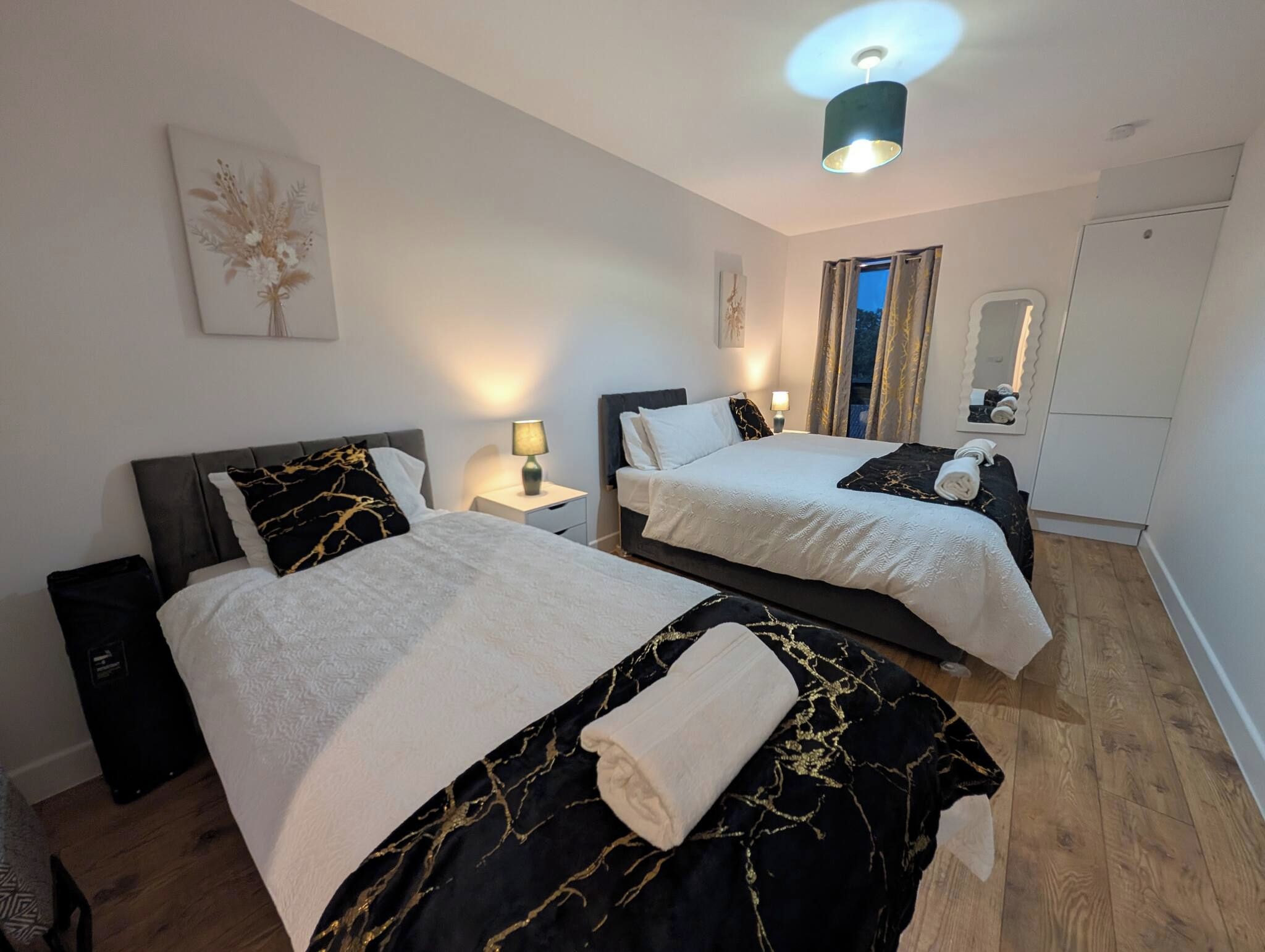 Ein Hotelzimmer mit zwei Betten, einem Nachttisch, einer Lampe, einem Spiegel und einer Deckenleuchte.