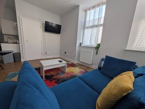 Ein modernes Wohnzimmer mit einem blauen Sofa, einem weißen Couchtisch und einem farbenfrohen Teppich.