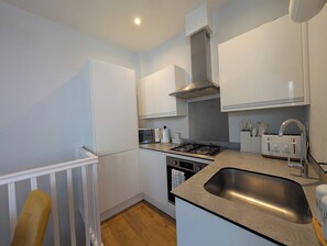 A modern kitchen with white cabinetry, a stainless steel sink, a gas stove, and a microwave. - Harbour Nest by Folkestone Harbour Arm (Folkestone)