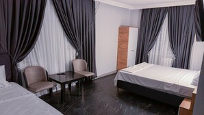 Quarto de hotel com cama, escrivaninha, duas cadeiras e um guarda-roupa.