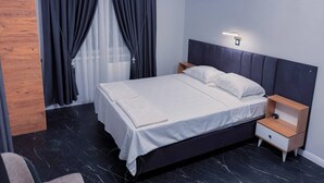 Quarto moderno com cama, mesas de cabeceira, painel de madeira e janela com cortinas.