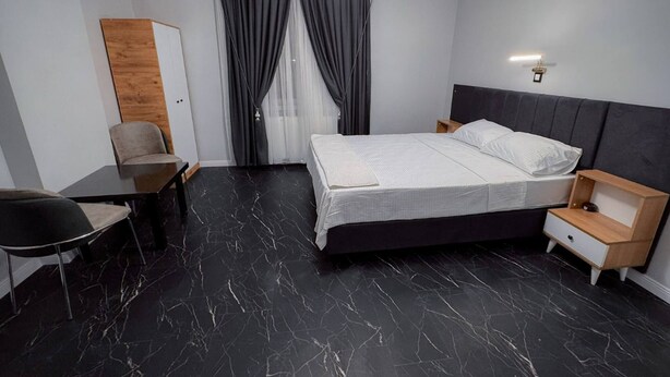 Quarto de hotel moderno com cama, escrivaninha, cadeira e mesa de cabeceira.