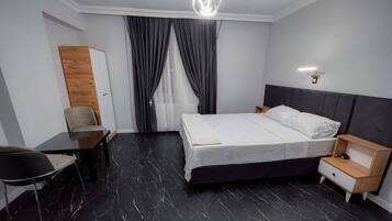 A modern hotel room with a bed, a desk, a chair, and a nightstand.