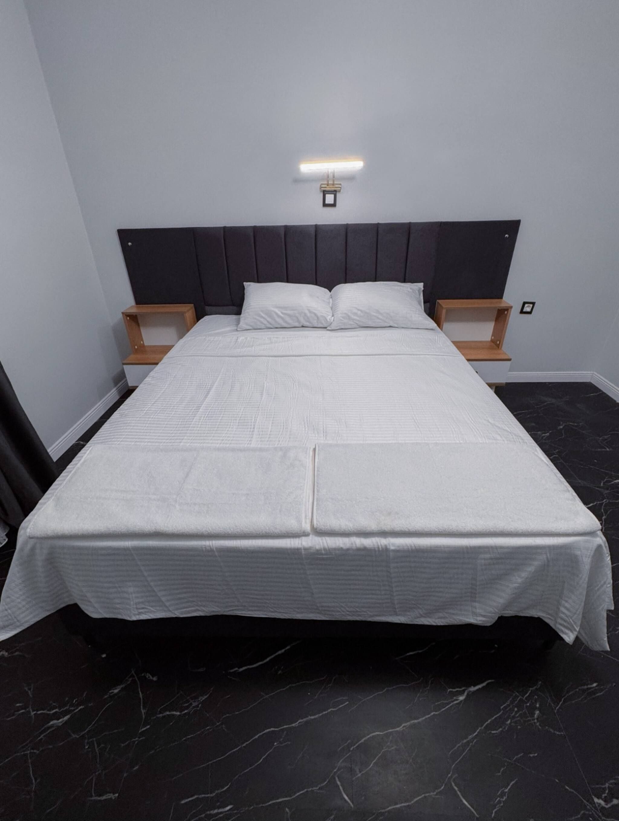 Un lit avec une tête de lit, deux tables de chevet et un luminaire fixé au mur.