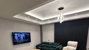 Uma sala de estar moderna com televisão de tela plana, sofás verdes e brancos, uma mesa de centro e um tapete preto decorativo.