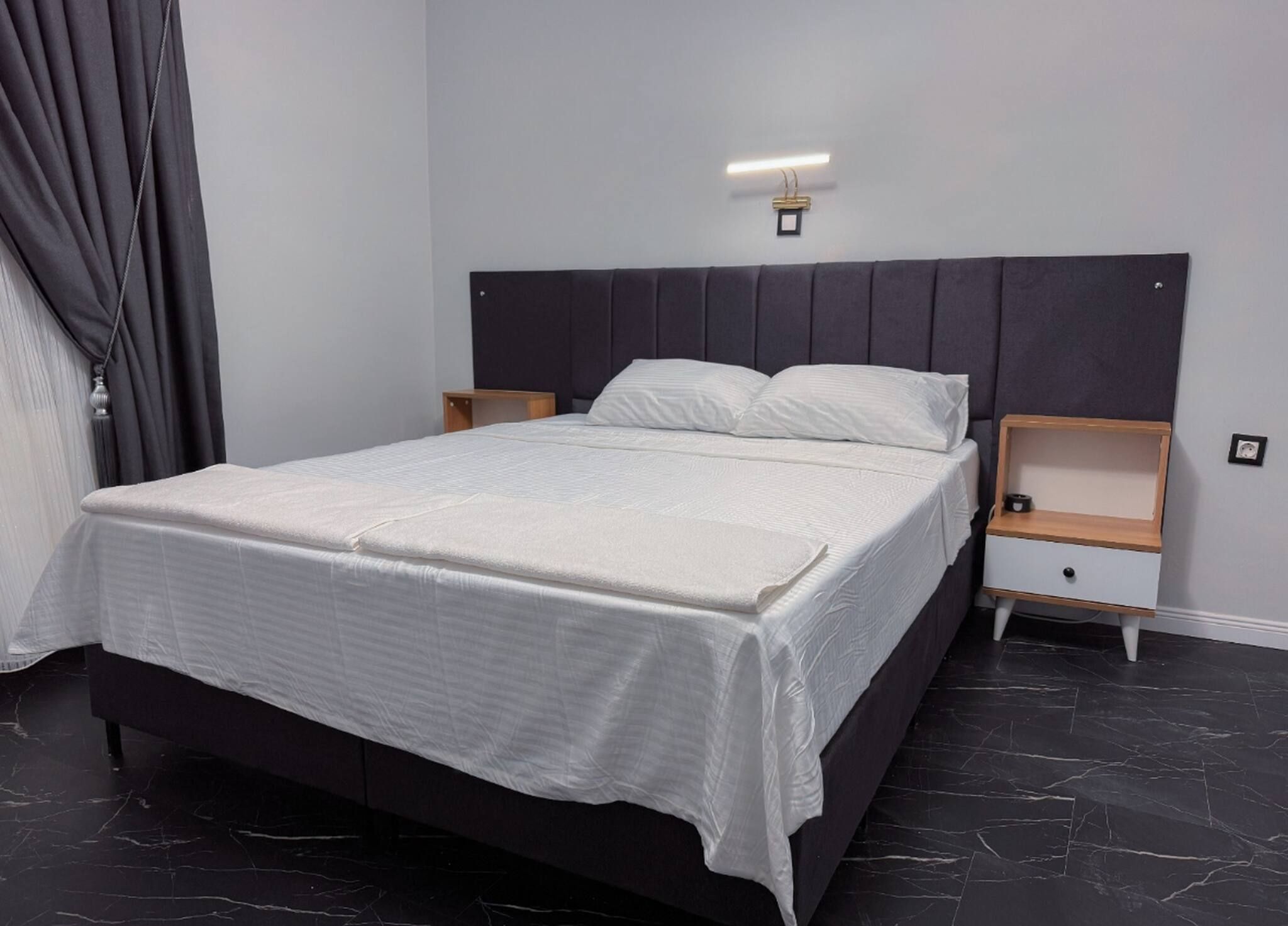 Une chambre moderne avec un grand lit, deux tables de chevet et une tête de lit dotée d’un éclairage intégré.