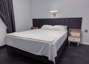 Une chambre moderne avec un grand lit, deux tables de chevet et une tête de lit dotée d’un éclairage intégré.