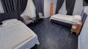 Quarto de hotel com duas camas, uma escrivaninha e uma cadeira.