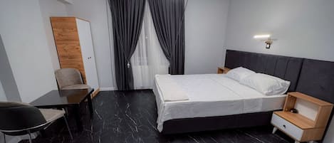 A modern hotel room with a bed, bedside table, chair, and a desk.