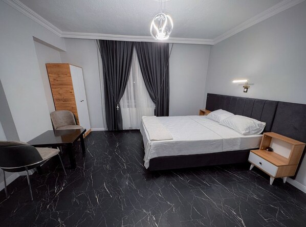 A modern hotel room with a bed, bedside table, chair, and a desk.